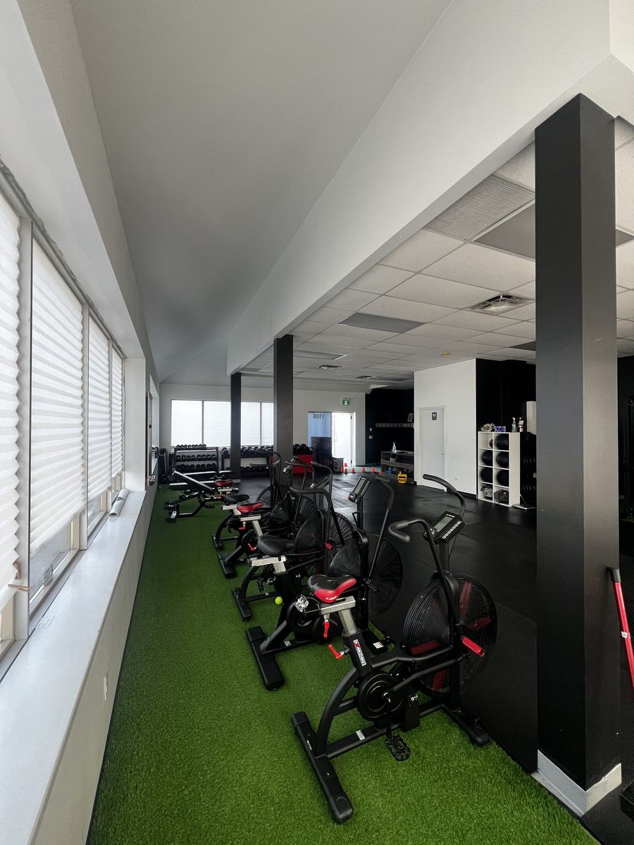 A row of air bikes on turf beside the windows on the TCT Gym conditioning side.